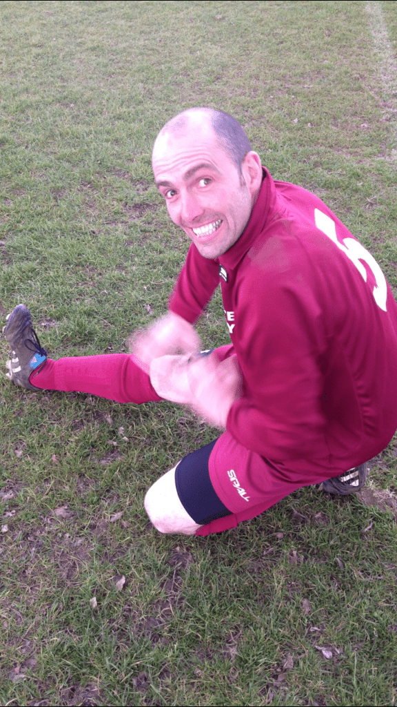 Alan Hyslop wearing maroon sportswear stretching on the grass.
