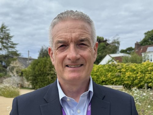 John G Burns, the man is wearing a suit jacket and shirt with his top button undone.