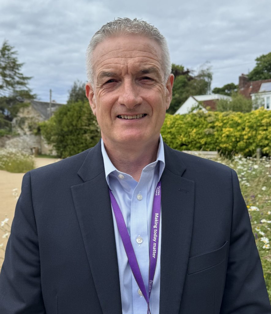 John G Burns, the man is wearing a suit jacket and shirt with his top button undone.